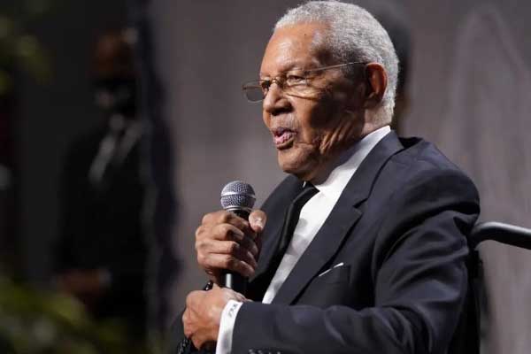 Andy Achenbaum smiling in a navy suite with a brightly patterned tie standing in a feild